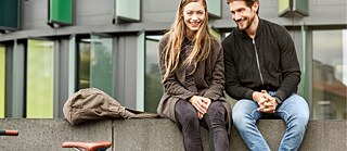 Eine junge Frau und ein junger Mann sitzen lächelnd zwischen zwei geparkten Fahrrädern