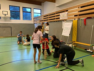 Jugendliche in einer Turnhalle bauen Türme aus Holzklözchen.