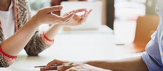 Nahaufnahme von Händen zweier Studierender. Vor ihnen liegen aufgeschlagene Bücher.