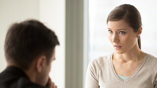 Eine junge Frau blickt einen Mann fragend an, der ihr gegenüber sitzt