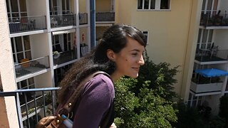 Die junge Frau Nevin sieht von einem Balkon nach unten und lächelt.