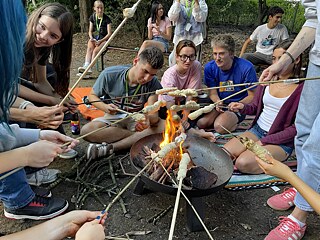Jugendliche backen Stockbrot um ein Lagerfeuer