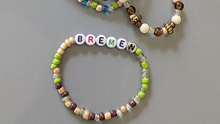 Armbänder aus künstlichen Perlen, auf einem steht „Bremen“ in bunten Lettern.