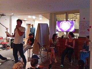 Jugendliche sitzen zusammen in einem Raum, jemand spricht ins Mikrofon.