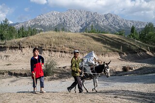 A man walks with a girl through Kök-Tash village, Kyrgyzstan. A donkey carries bags filled with dry dung.