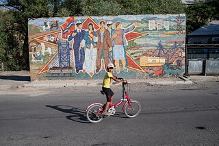 A boy rides a bicycle in front of a mosaic at the center of Sülüktü city, Kyrgyzstan.
