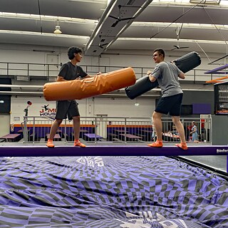 Jugendliche auf einem Schwebebalken, darunter liegt eine dicke Matte.