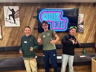 Drei Jugendliche vor einem Bildschirm, auf dem „Quiznight“ steht.