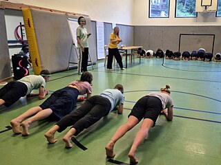 Junge Menschen in einer Sporthalle beim Unterarmstütz.