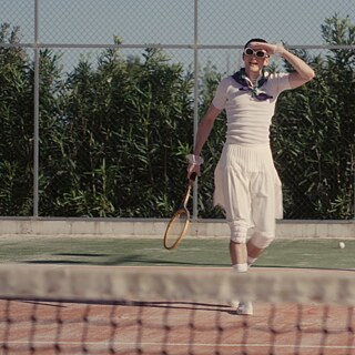 Schauspieler Sebastian Schneider im weißen Tenniskostüm mit Sonnenbrille und Schläger in der Hand