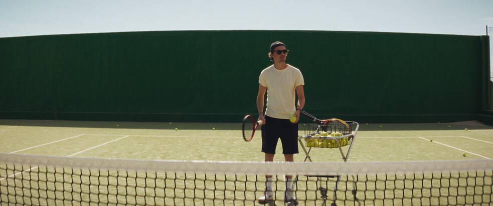 Tom auf dem Tennisplatz mit einem einem Wagen voller Tennisbälle.