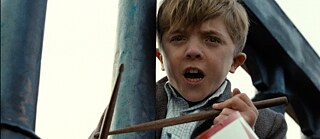 L’affiche très célèbre du film Le Tambour fait un gros plan sur le visage du jeune Oskar passant la tête entre les barreaux d’une rambarde, son tambour autour du cou et ses baguettes à la main. 