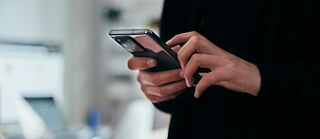 A set of hands holding a phone. In the background blurred is a workstation visible