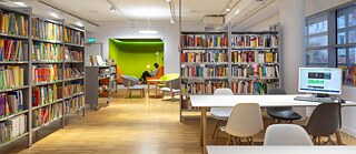 hell erleuchteter Bibliotheksraum mit Büchern, Computertischen und gemütlicher Leseecke