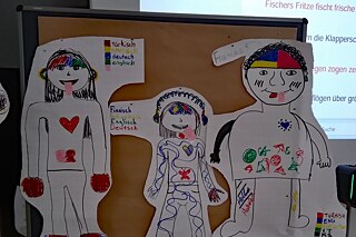 Figuren an einer Pinnwand, im Hintergrund werden Zungenbrecher projeziert.