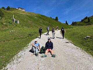 Jugendliche sitzen erschöpft auf einem Wanderweg.