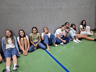 Jugendliche sitzen auf dem Boden einer Sporthalle.