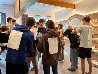 Jugendliche schreiben auf Zettel, die andere auf dem Rücken tragen.