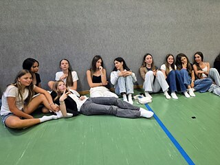 Jugendliche sitzen auf dem Boden einer Sporthalle.