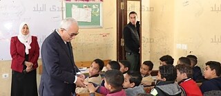 Ein Pädagoge steht in einem Klassenzimmer neben einer Gruppe sitzender und aufmerksamer Schüler.     ChatGPT fragen