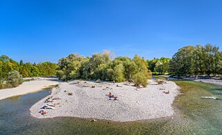 Ein Kiesstrand an einem Fluss. Personen sonnen sich am Ufer.