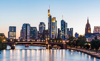 Große Bürogebäude entlang eines Flusses bei Sonnenuntergang. Die Gebäude werden von innen und außen beleuchtet.