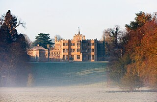 An English country house shrouded in fog, surrounded by trees and lawns.