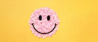 Smiley face made of pink flower petals on a yellow background. &copy; © Unsplash Adapting Abroad