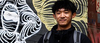 A young man in front of a graffitied wall