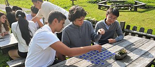 Jugendliche sitzen an einem Holztisch auf dem ein Memory ausgelegt ist.