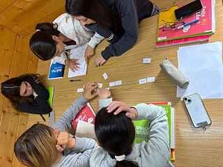 Jugendliche sitzen um einen Tisch und fügen Papierschnipsel aneinander.