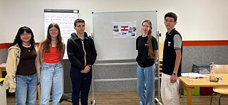 Jugendliche stehen vor Tafel und Flipchard in einem Klassenraum.