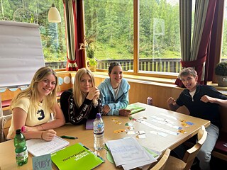 Jugendliche sitzen an einem Tisch und setzen Papierschnipsel zusammen.