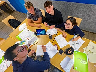 Jugendliche sitzen vergnügt um einen Tisch und lernen.