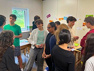 Jugendliche stehen zusammen in einem Unterrichtsraum und unterhalten sich.