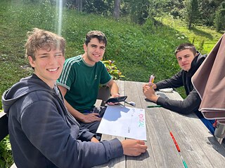 Jugendliche sitzen im Freien an einem Tisch und malen ein Plakat.