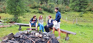 Jugendlliche sitzen um eine erloschenes Lagerfeuer in den Bergen.