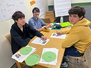 Jugendliche sitzen um einen Tisch und lernen.