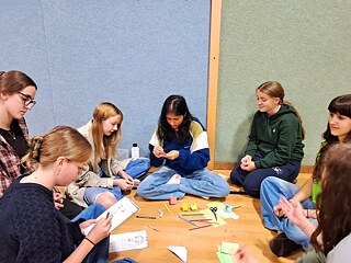 Jugendliche sitzen auf dem Fußboden und basteln und portraitieren.