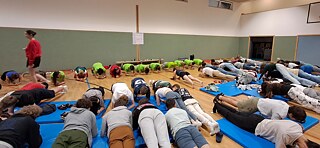 Junge Menschen in einer Sporthalle bei der Unterarmstütz-Übung