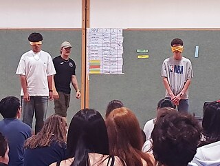 Zwei Jugendliche haben die Augen verbunden, andere beobachten das Geschehen.