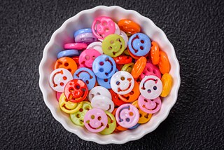 A medium-sized, white porcelain bowl stands on a black background. This is filled with colorful plastic smileys.