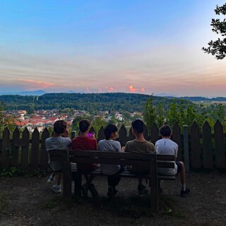 Jugendliche auf einer Parkbank blicken bei Sonnenuntergang auf eine Stadt, oder auf ihr Smartphone.