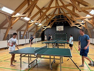 Jugendliche spielen Tischtennis in einer großen Sporthalle.