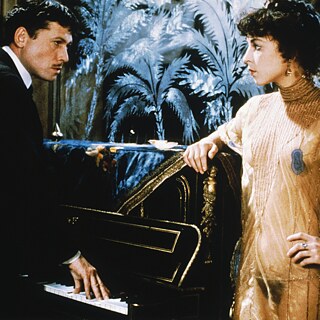 Ein Mann an einem Klavier und eine Frau in einem durchsichtigen Kleid