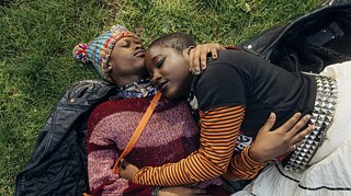 Lotta (Vanessa Yeboah, right) and Kojo (Thapelo Mashiane, left), lying entwined on the grass.
