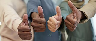 Vier Personen zeigen ihren nach oben gestreckten Daumen in Nahaufnahme. 