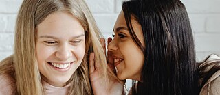 Zwei Mädchen flüstern sich etwas zu. 