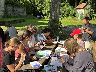 Jugendliche malen an einem Tisch in einem Park.