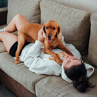 Ein Mädchen liegt mit einem Hund auf einer Couch.